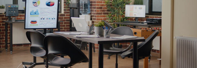 Una mesa con sillas muestra un gráfico en un atril, en una zona exterior de ladrillo con plantas.