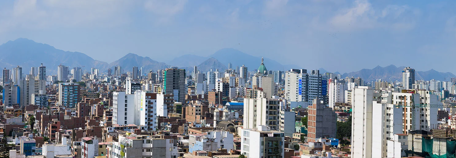 Una extensa ciudad se extiende sobre un paisaje montañoso, con edificios de diversos tamaños y alturas. Los edificios altos destacan sobre una densa colección de estructuras más bajas.