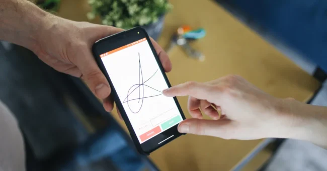 Una persona firma con el dedo en un celular que sostiene otra